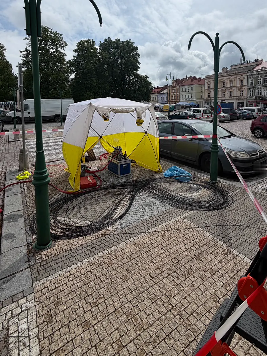 Optický kabel složený do osmičky na dlažbě náměstí, za ním žlutobílý svařovací stan