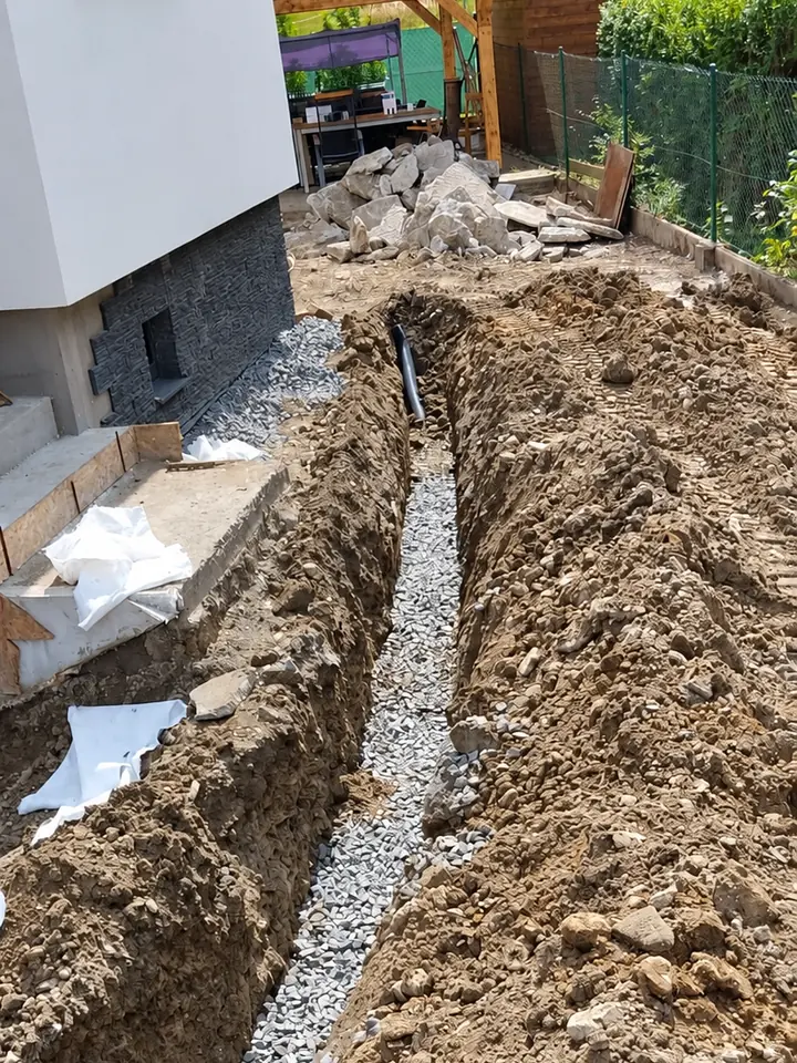 Dlouhá rýha se štěrkovým ložem podél rodinného domu, na konci napojené potrubí